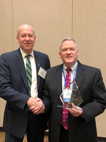 mg-caption: Gerald Wojtala, executive director of IFPTI presented the award to Joel Kuplack, senior vice president of HR, who accepted the award on behalf of Skogen’s Festival Foods at the Food Safety Committee Meeting in Phoenix. 