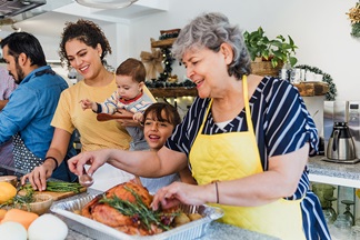 Multi generational family preparing a meal of turkey and vegetables in a kitchen.