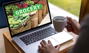 Person drinking coffee looking at a grocery online site on a laptop